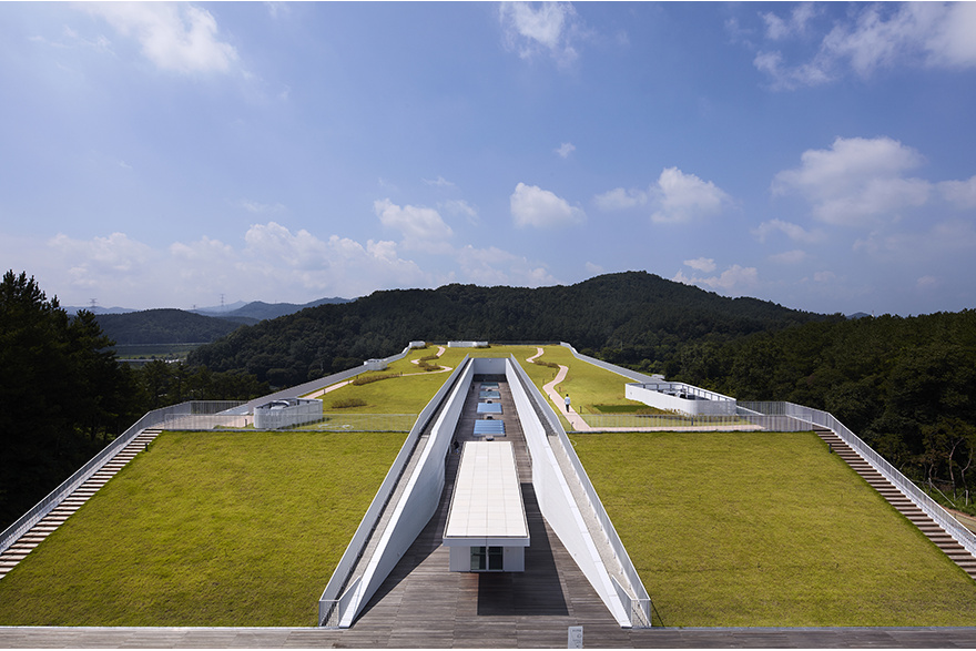 Green roof with a central skylit walkway, framed by forested hills