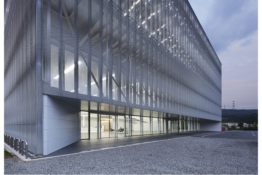 Silver mesh facade at dusk with glowing glass ground floor