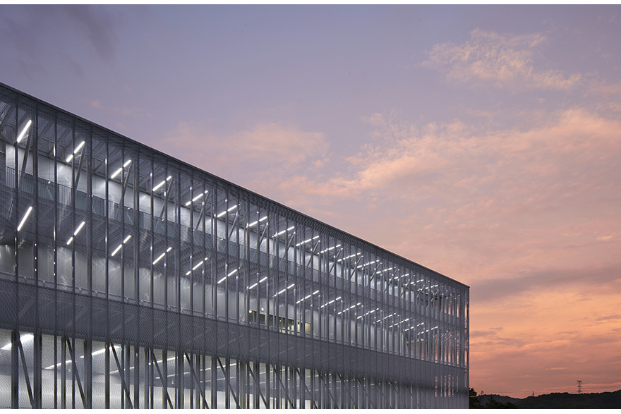 Mesh facade lit from within against a pink sunset sky