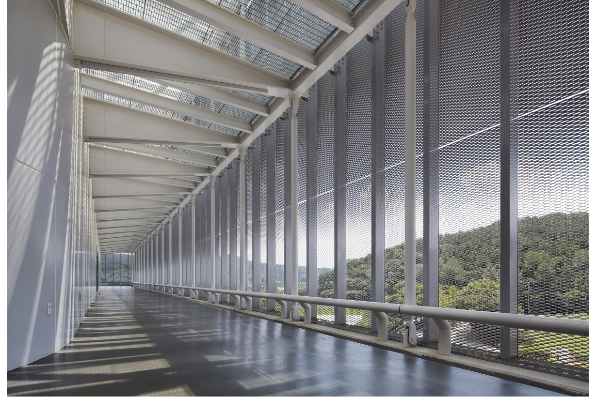 Daylit corridor with mesh screen walls and forest views