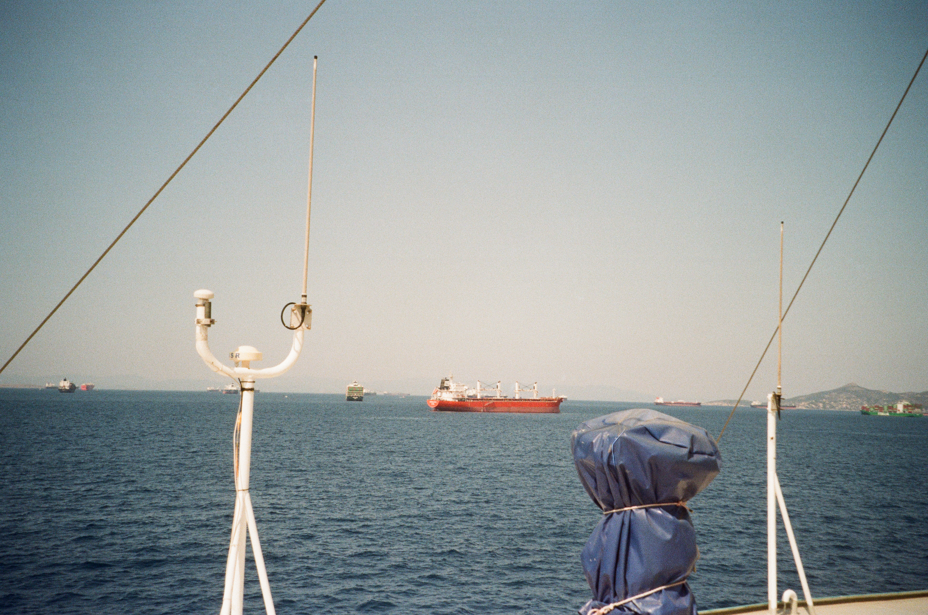 Cargo ships at sea seen past a boat's antenna