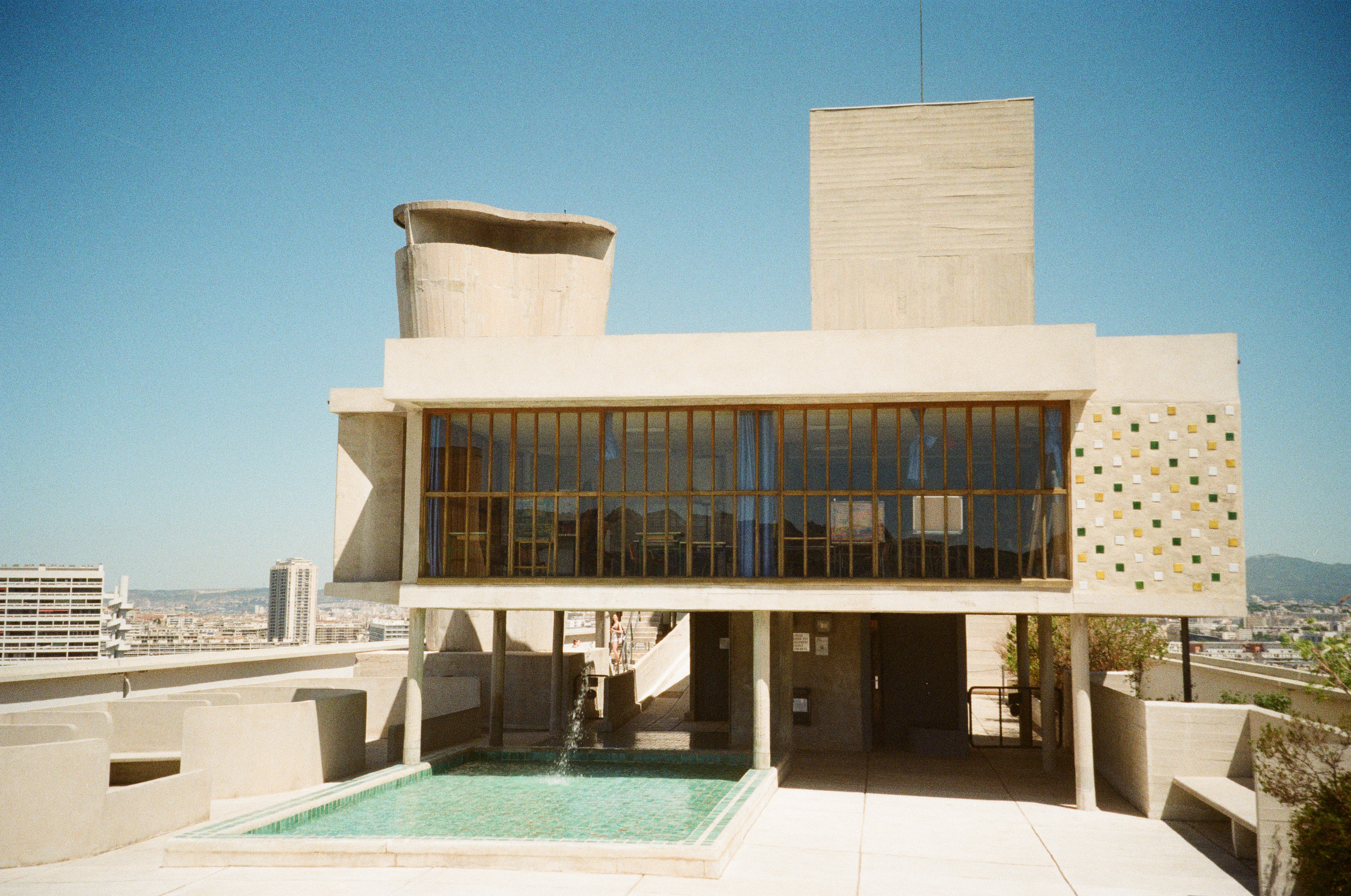 Concrete rooftop pavilion on slender pillars with a tiled pool