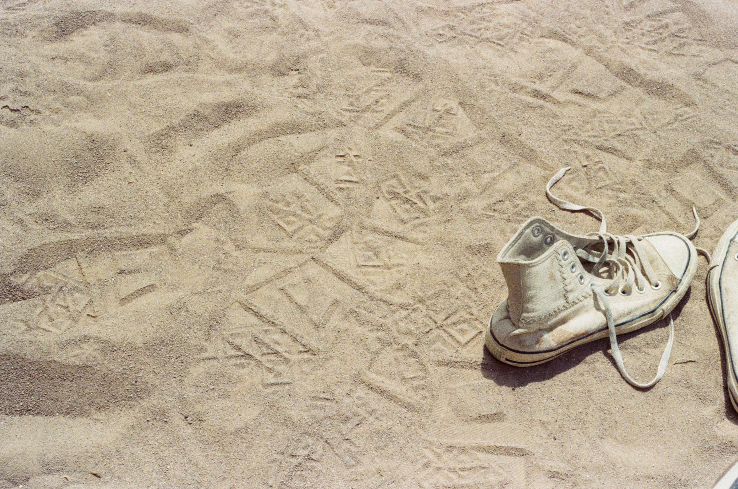 Worn white high-top sneaker on sand covered in footprints