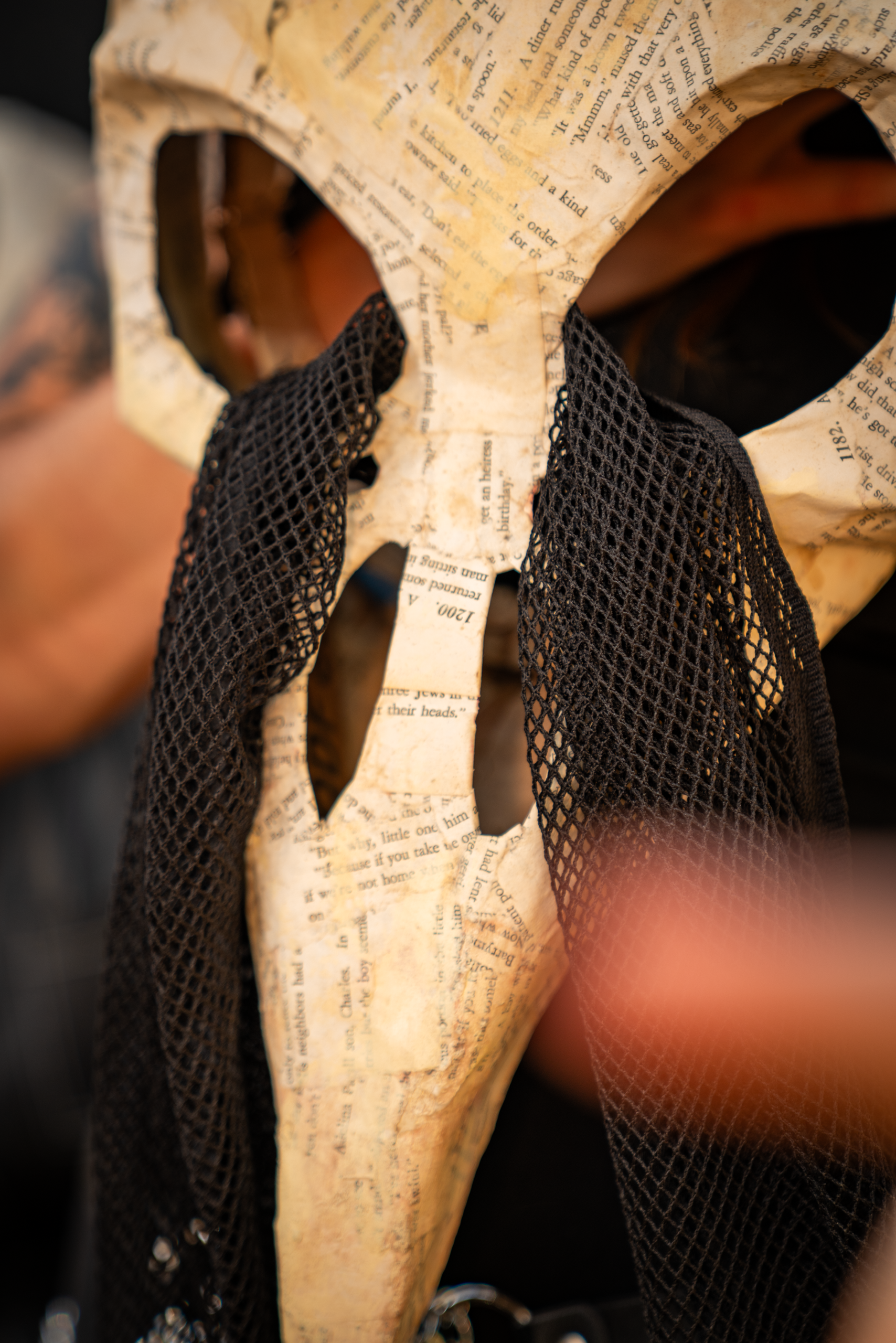 Paper-mache bird-skull mask covered in book pages, with a black mesh veil