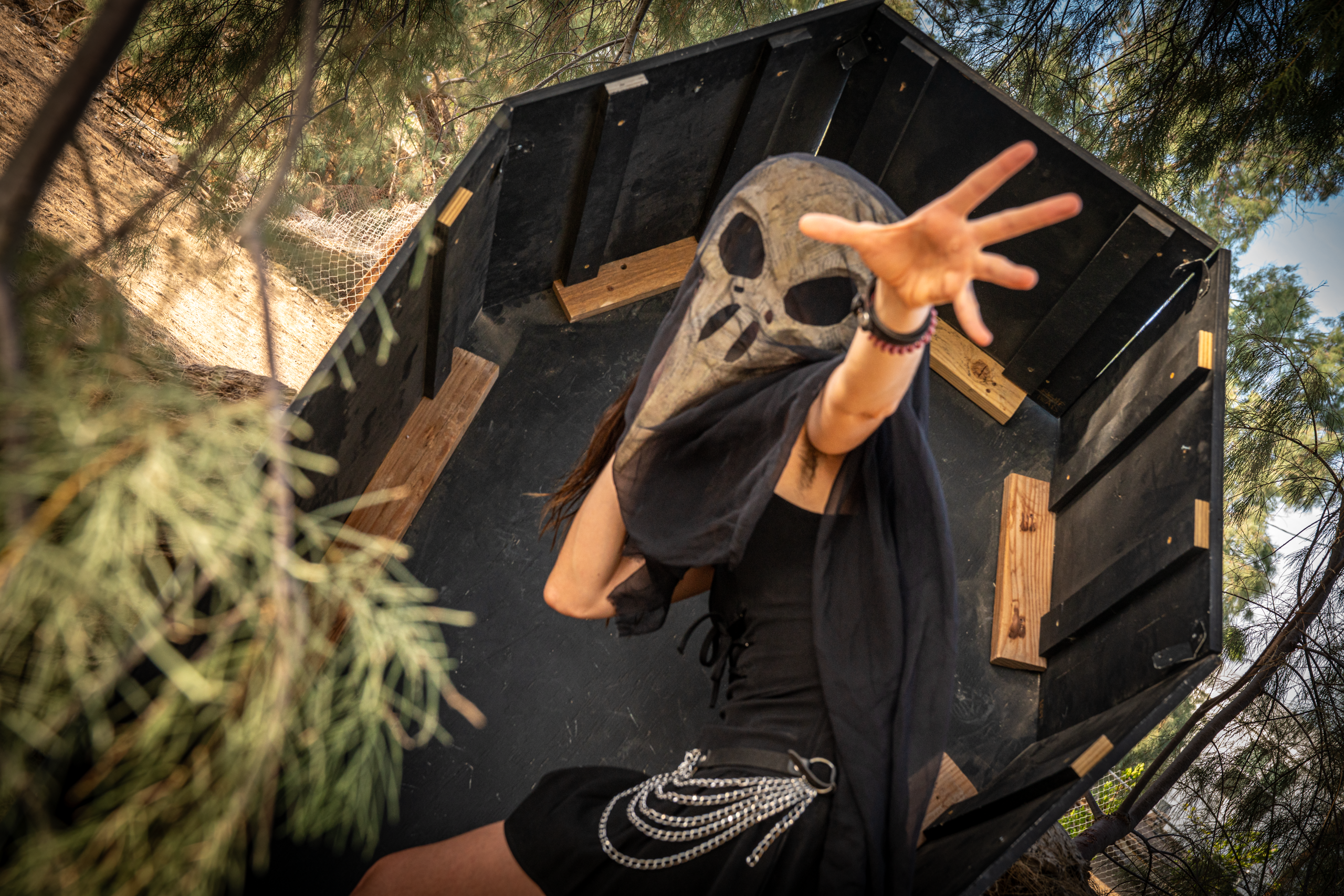 Masked figure in a sheer black veil reaching toward the camera from inside an open black coffin